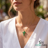 Woman wearing a gold necklace with a green pendant, blurred outdoor background