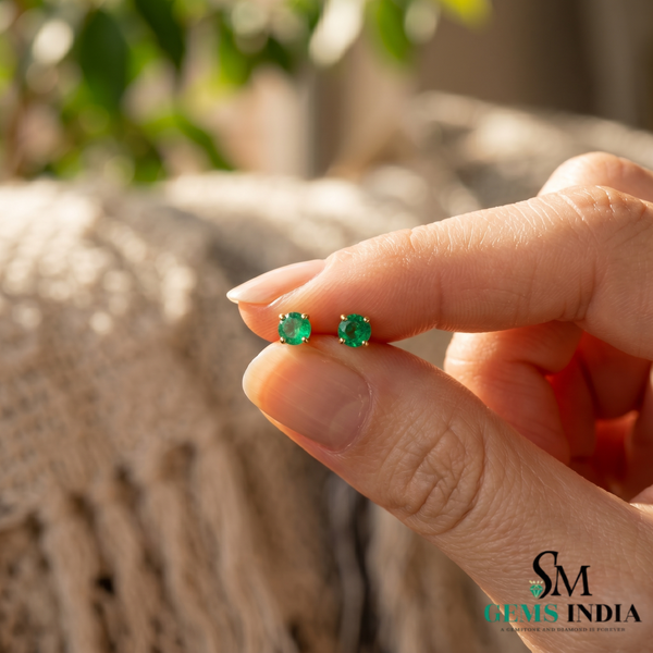 Small round emerald stud earrings held between fingers in natural light, minimalist women’s jewellery design