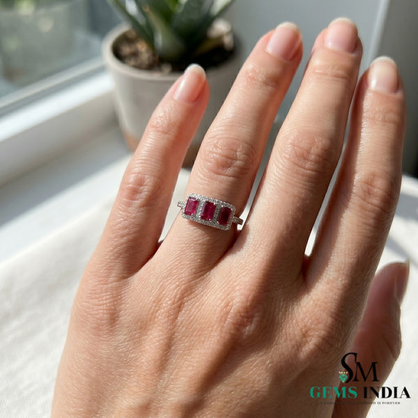 Hand wearing a ring with red gemstones against a neutral background